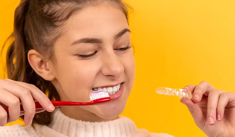 Girl Holding Invisalign Tray While Brushing Teeth